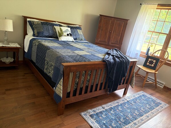 A bedroom with a wooden bed, a nightstand, a dresser, and a window with curtains.