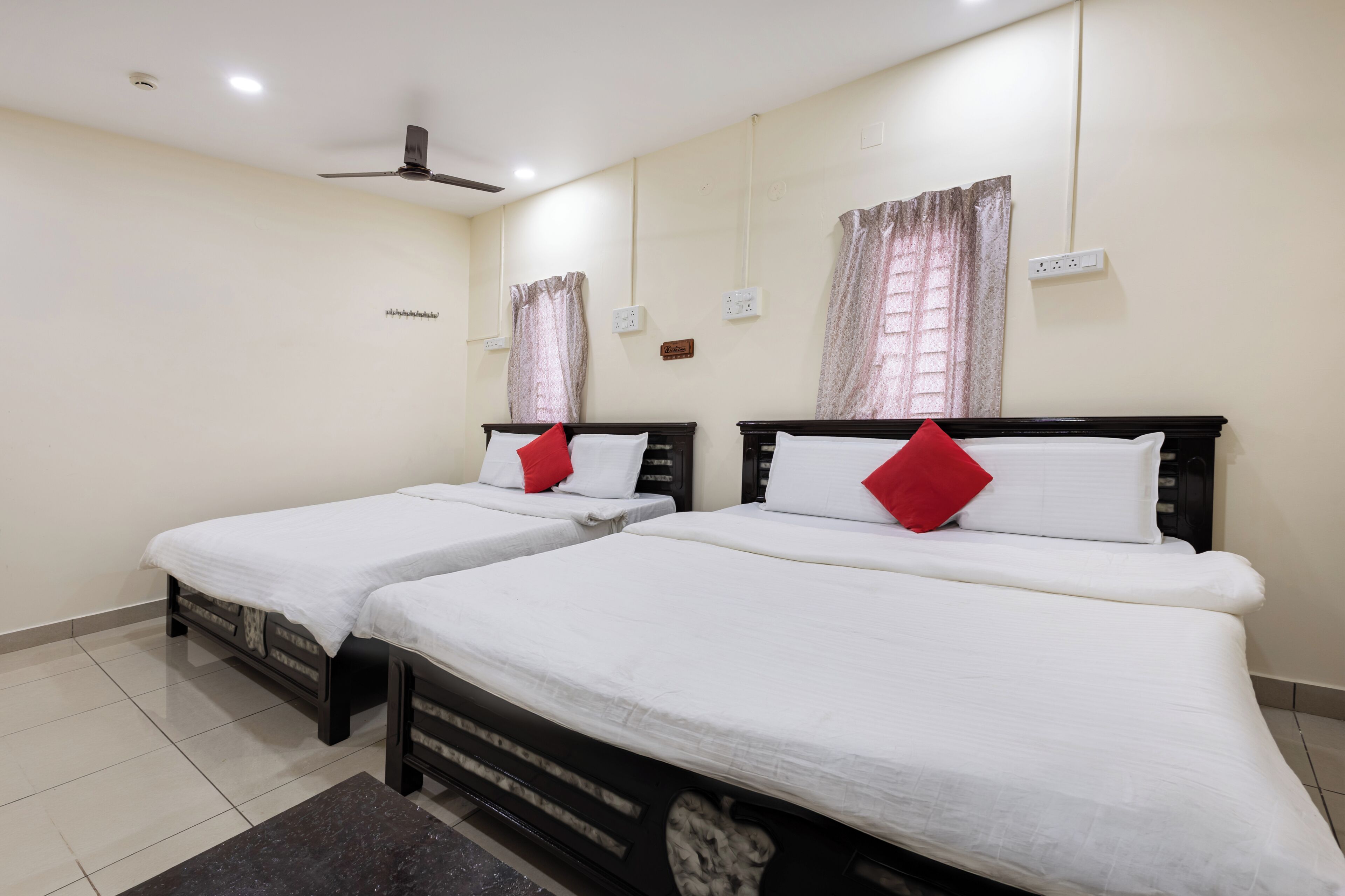Habitación de hotel con dos camas, ventilador de techo y ventana con cortinas.
