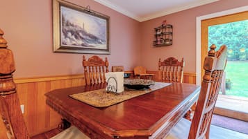 Un comedor con una mesa de madera, sillas, un cuadro y vistas al exterior.
