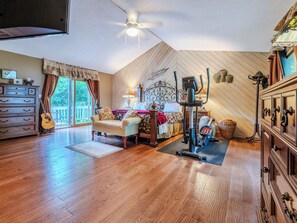 A bedroom with a bed, a guitar, a ceiling fan, and a workout machine. - Beautiful Home on Mountainous Tree Farm (Newland)
