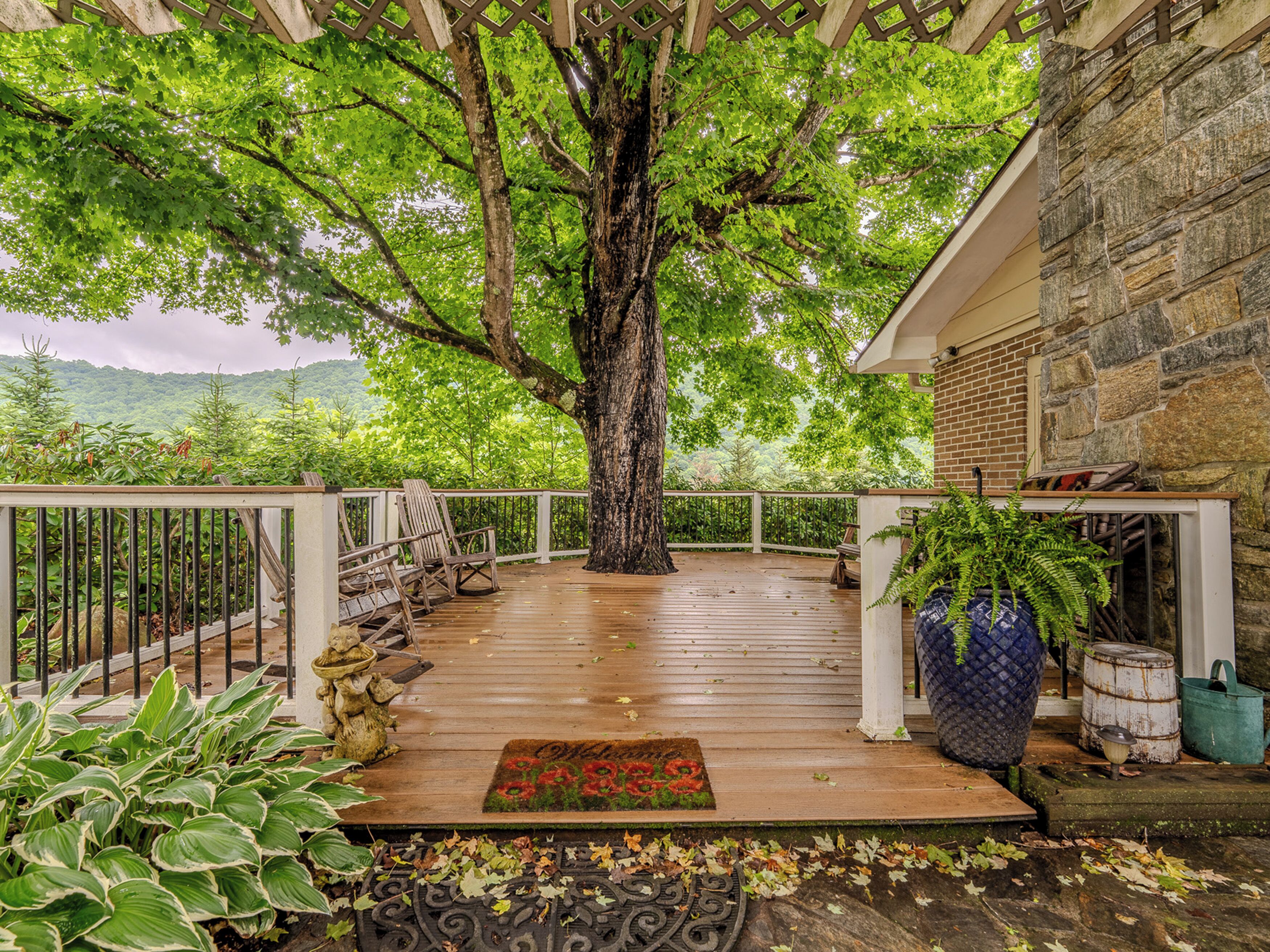 A wooden deck with a white railing, a large tree, and a stone building in the background.