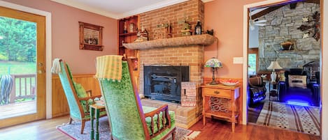 A cozy living room with a fireplace, a green armchair, a wooden coffee table, and a stone fireplace surround.