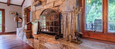 A stone fireplace with a glass door, a wooden mantel, and a window with a view of trees.