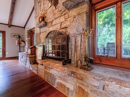 Una chimenea de piedra con puerta de cristal, una repisa de madera y una ventana que da a los árboles.