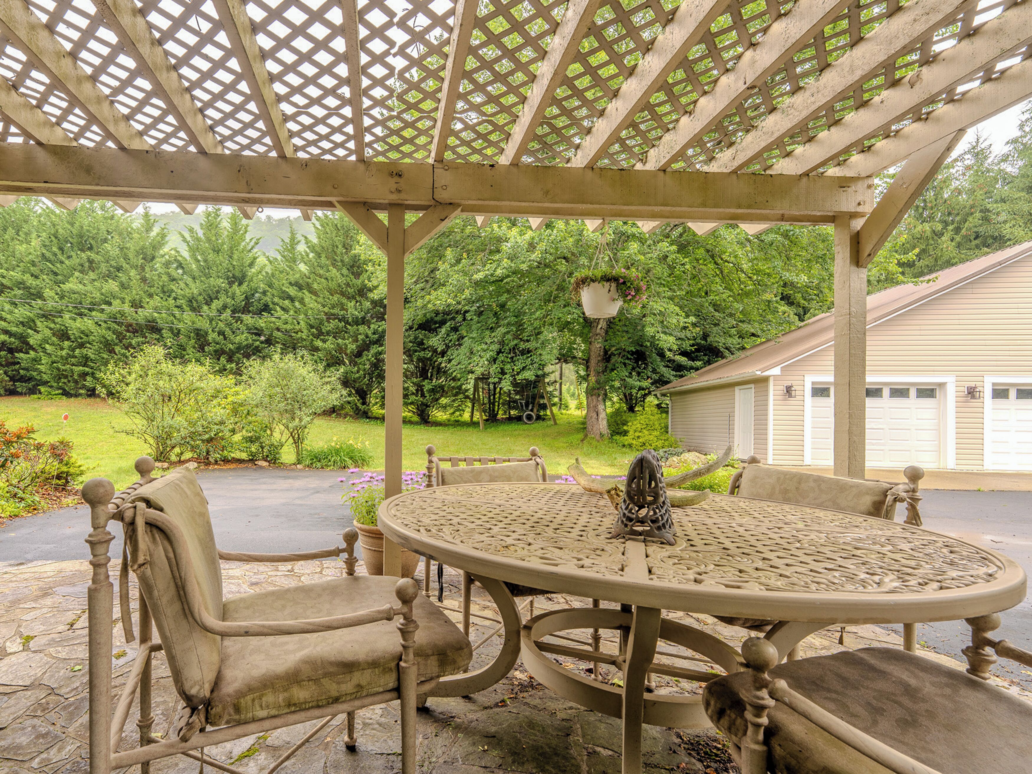 A covered outdoor seating area with a round table and chairs, surrounded by a wooden lattice structure.