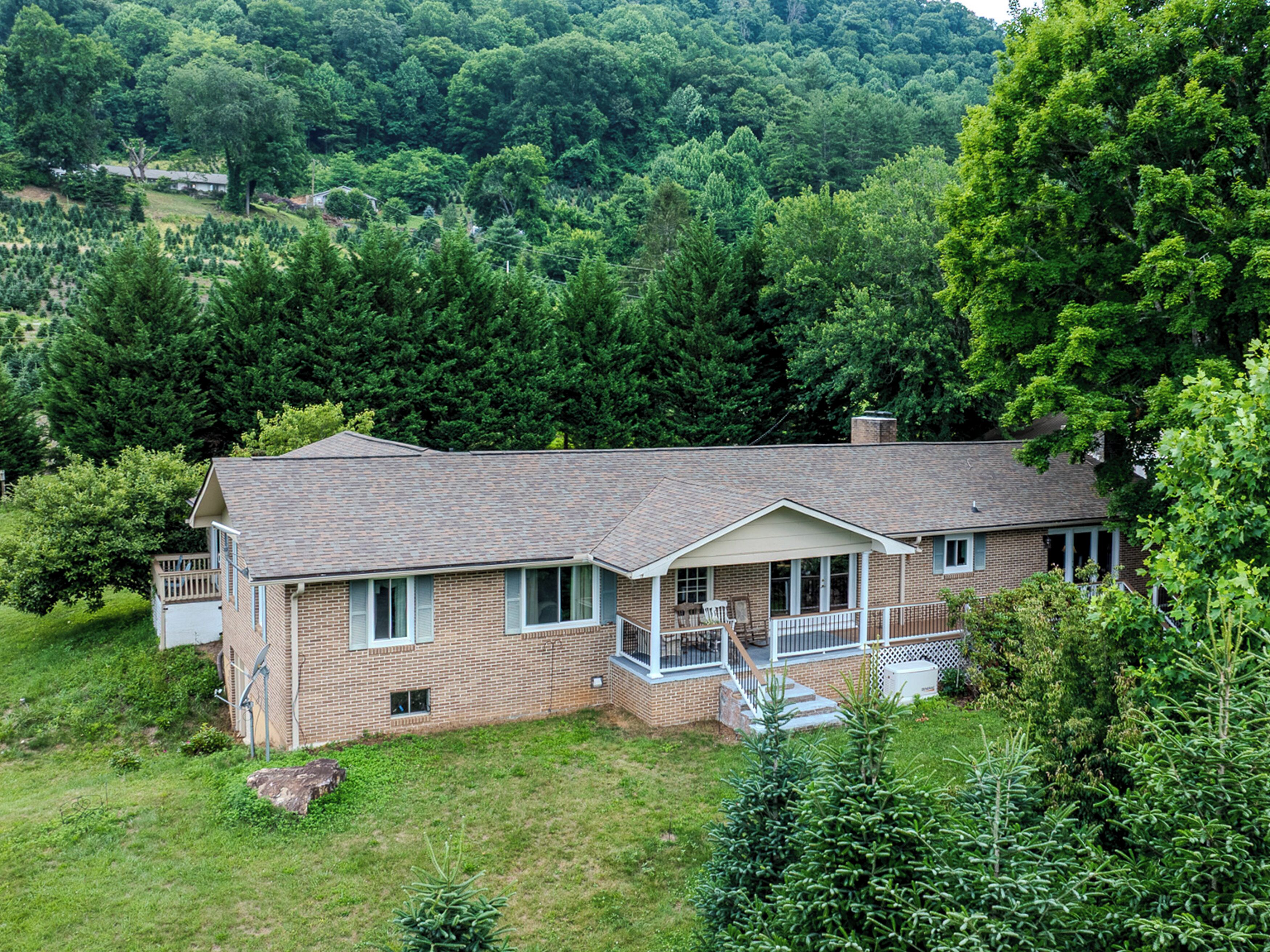 A two-story house with a front porch, surrounded by dense forest.