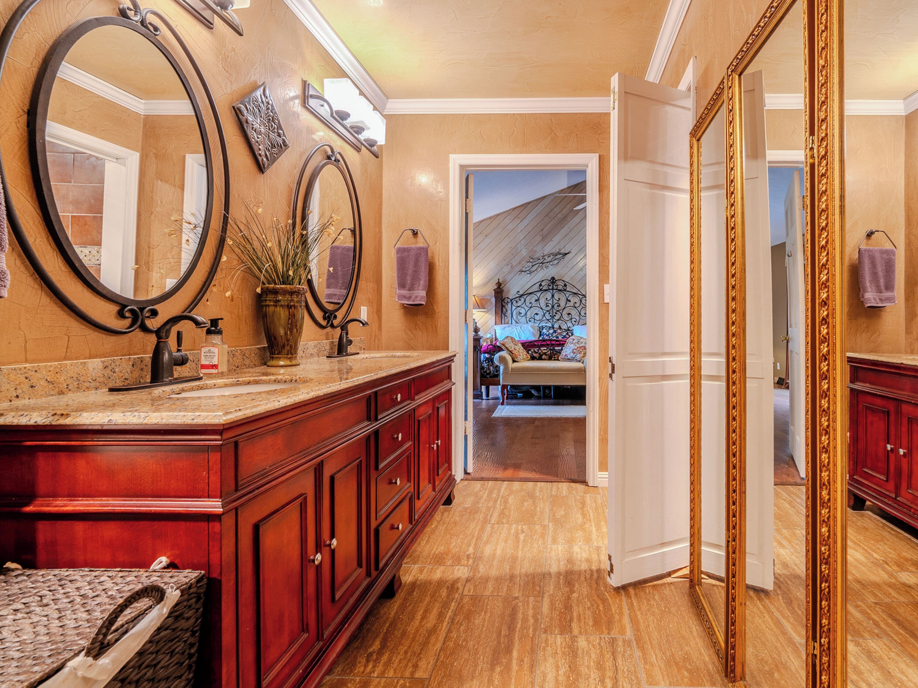 A hallway with a vanity, mirrors, and a bed in the background.