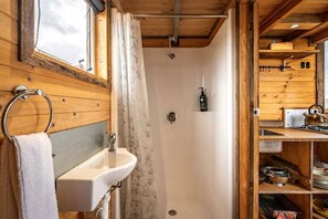 Interior de una cabaña de madera con un baño que incluye un lavamanos, ducha e inodoro.
