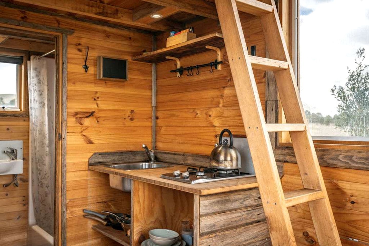Interno di una baita in legno con angolo cottura, che include un lavello, un fornello, un bollitore e una scala.