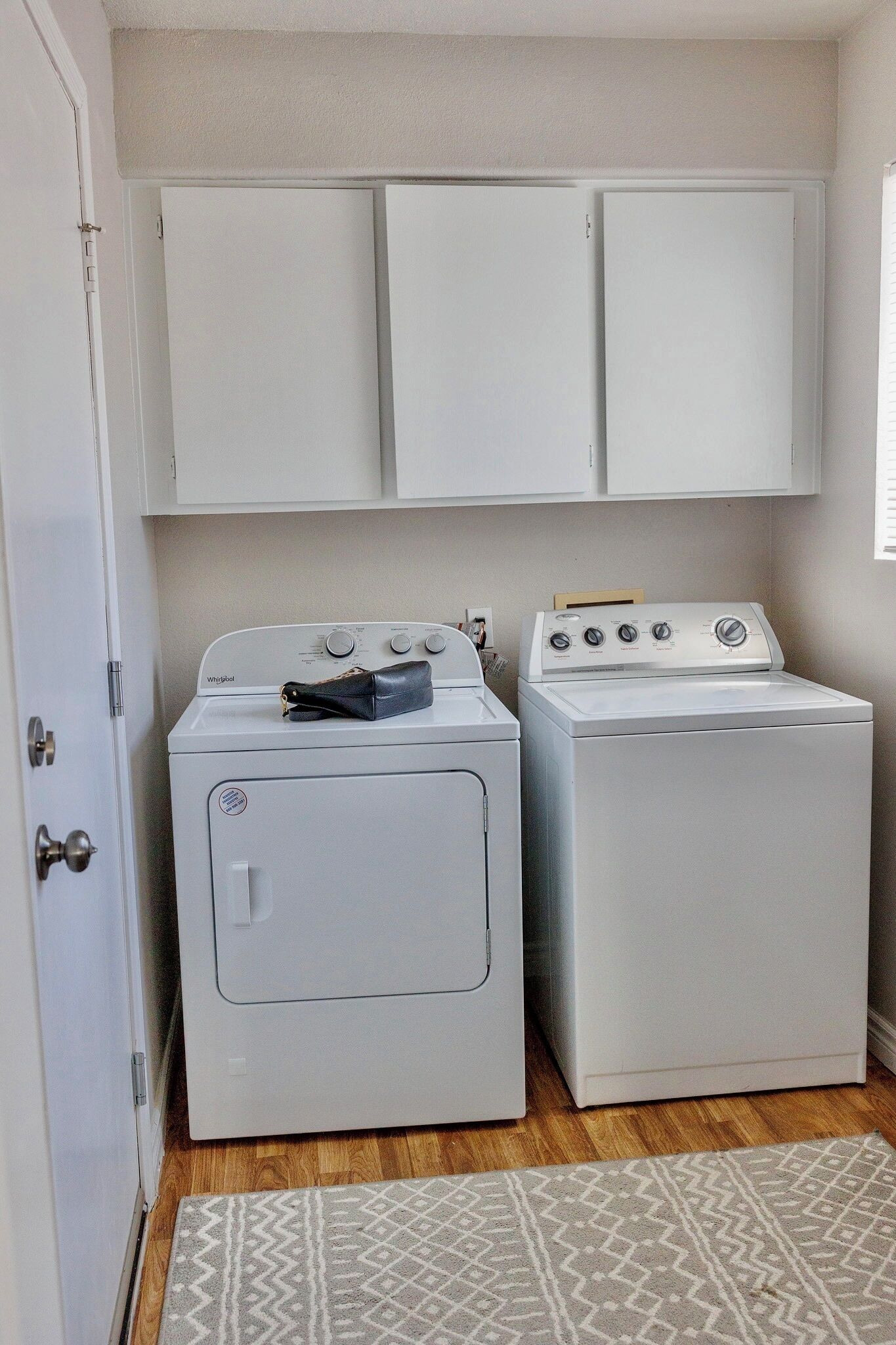 A laundry area with two white washers and dryers, a wooden floor, and a patterned rug.