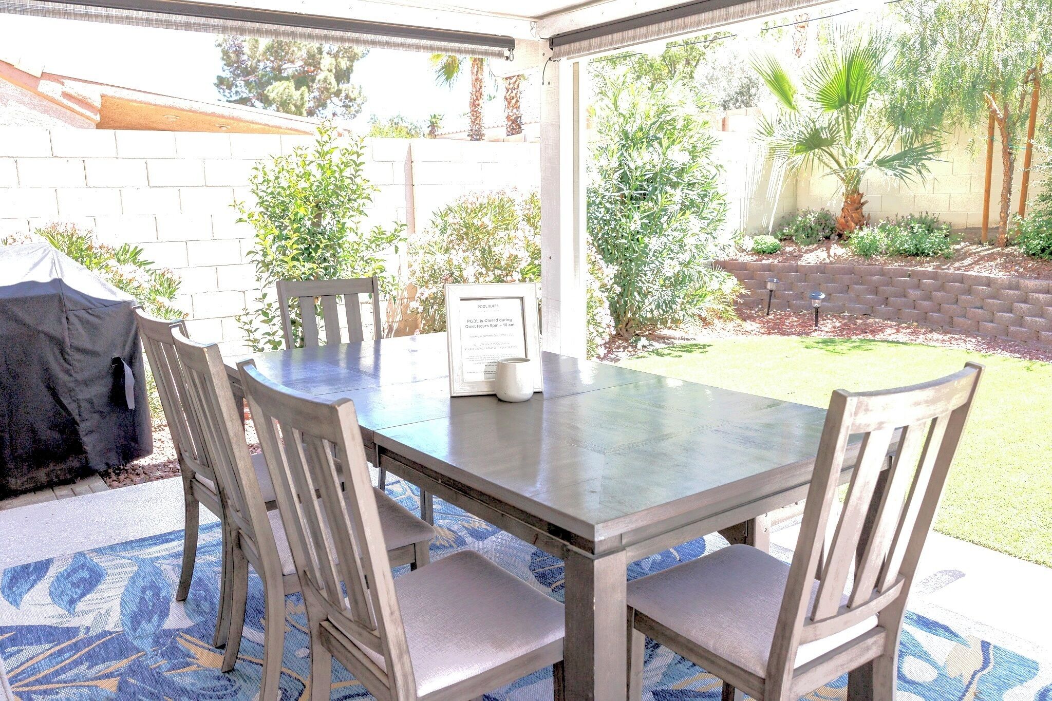 A covered patio with a table and chairs, surrounded by a brick wall and various plants.