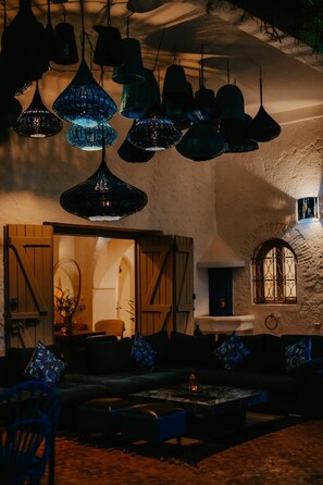 A cozy interior with hanging blue lamps, a fireplace, and a rustic stone wall. - Kasbah Amaya – 7 bedrooms, swimming pools, hammam & Atlas vue (Marrakech)