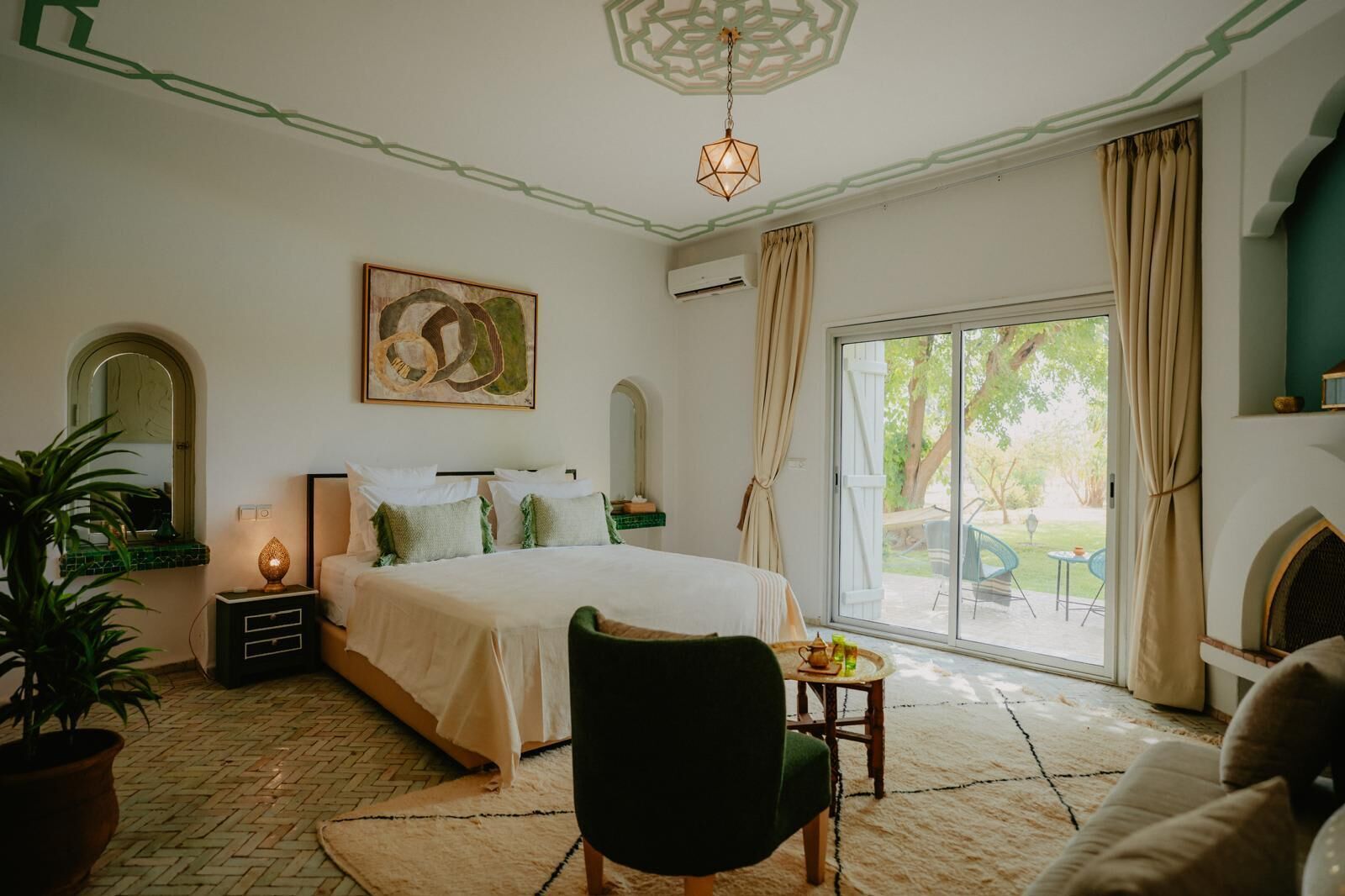 A bedroom with a large bed, a nightstand, a lamp, a chair, and a view of the outdoors through a sliding door.