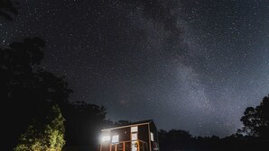 Una casa con un amplio ventanal, un porche y un cielo nocturno lleno de estrellas.