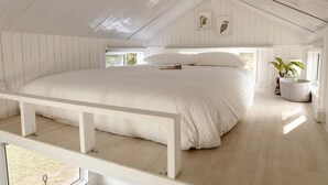 Amplia habitación con una cama grande, suelo de madera y ventana que deja entrar luz natural.