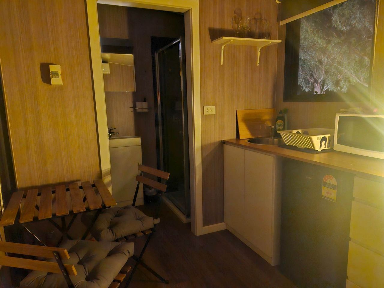 A compact room with a wooden bed, a small kitchenette, and a television mounted on the wall.