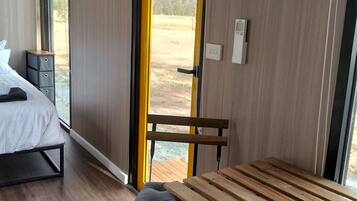 A modern room with a bed, a bench, and a table. There is a window with a view of the outdoors.