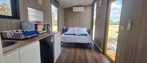 A compact room with a kitchenette, a bed, and a large window.