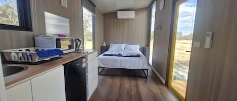 A compact room with a kitchenette, a bed, and a large window.