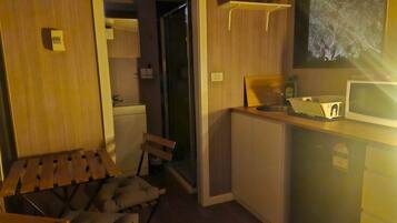 A compact room with a wooden bed, a small kitchenette, and a television mounted on the wall.