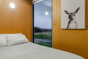 Une chambre à coucher avec un lit, une fenêtre donnant sur un paysage et un tableau représentant un kangourou accroché au mur.