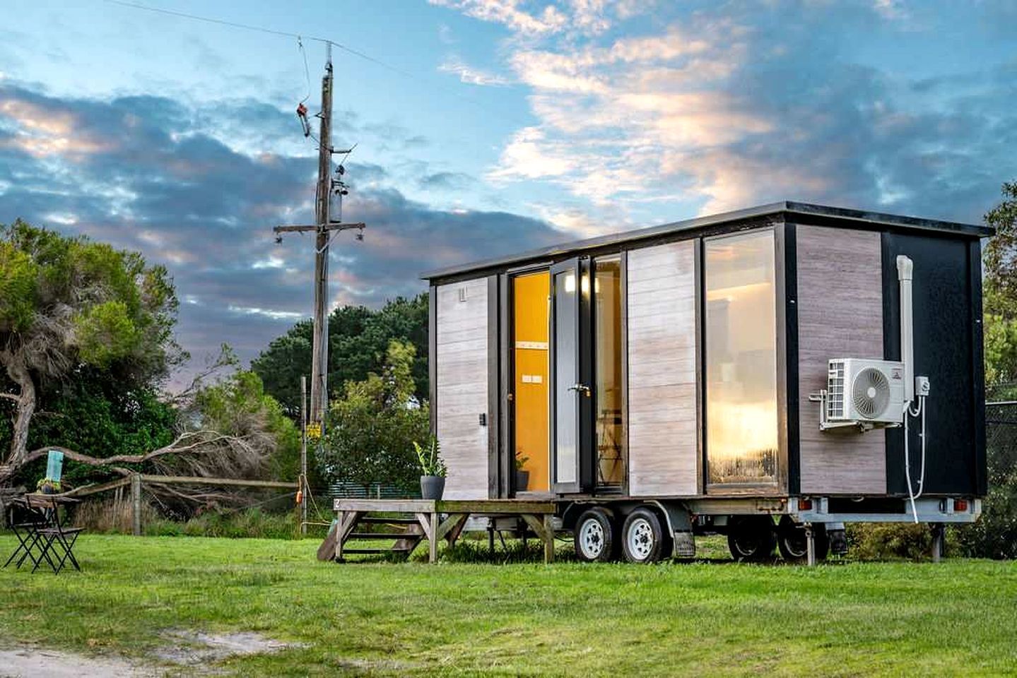 Une maison mobile dotée d’une porte coulissante, d’un petit porche et d’un appareil de climatisation mobile.