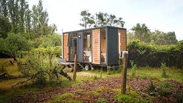 A modern, compact mobile home with a sliding door, situated in a lush, green environment.
