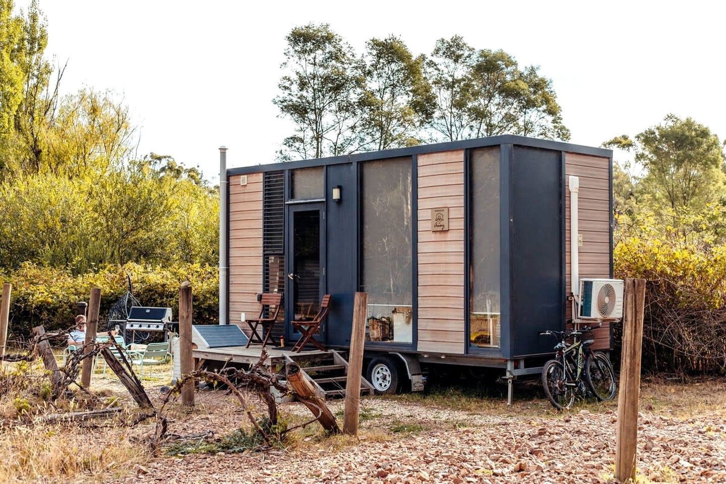 A compact mobile home with a large sliding door, a small porch area with seating, and a bicycle parked outside.