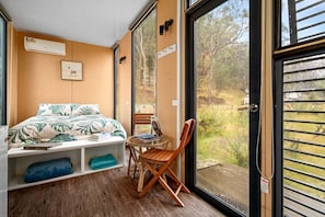 A bedroom with a bed, a chair, a table, a window, and a view of the outdoors.