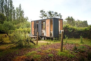 A modern, compact mobile home with a sliding door, situated in a lush, green environment.