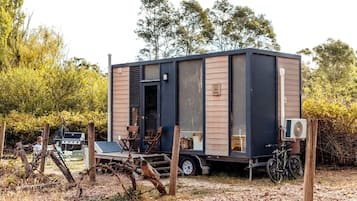 Una casa móvil compacta con un gran portón corredera, un pequeño porche con asientos, y una bicicleta estacionada afuera.