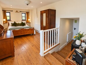 A bedroom with a wooden bed, a dresser, a nightstand, a mirror, a staircase, and a view of the outside. - The Farmers arms West Hatch (Taunton)