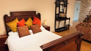 A neatly made bed with a wooden headboard, multiple pillows, a nightstand with a lamp, and a wooden bench with a basket.