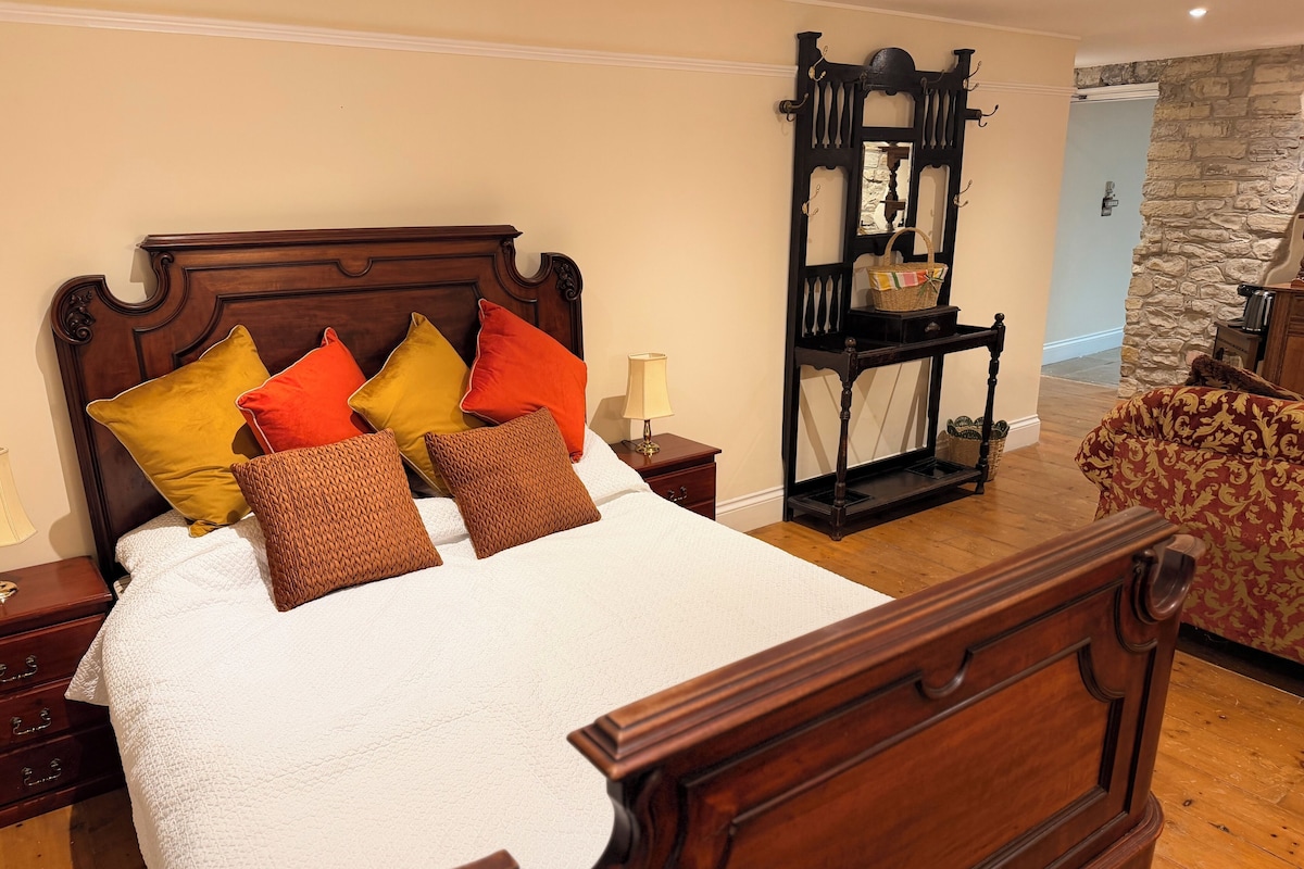 A neatly made bed with a wooden headboard, multiple pillows, a nightstand with a lamp, and a wooden bench with a basket.