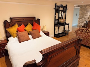 A neatly made bed with a wooden headboard, multiple pillows, a nightstand with a lamp, and a wooden bench with a basket.