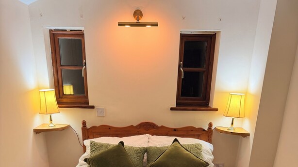 A bed with a wooden frame, two bedside lamps, and a green throw blanket.