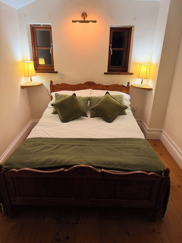 A bed with a wooden frame, two bedside lamps, and a green throw blanket.
