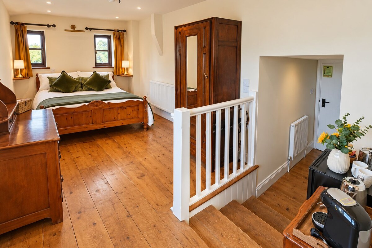 A bedroom with a wooden bed, a dresser, a nightstand, a mirror, a staircase, and a view of the outside.