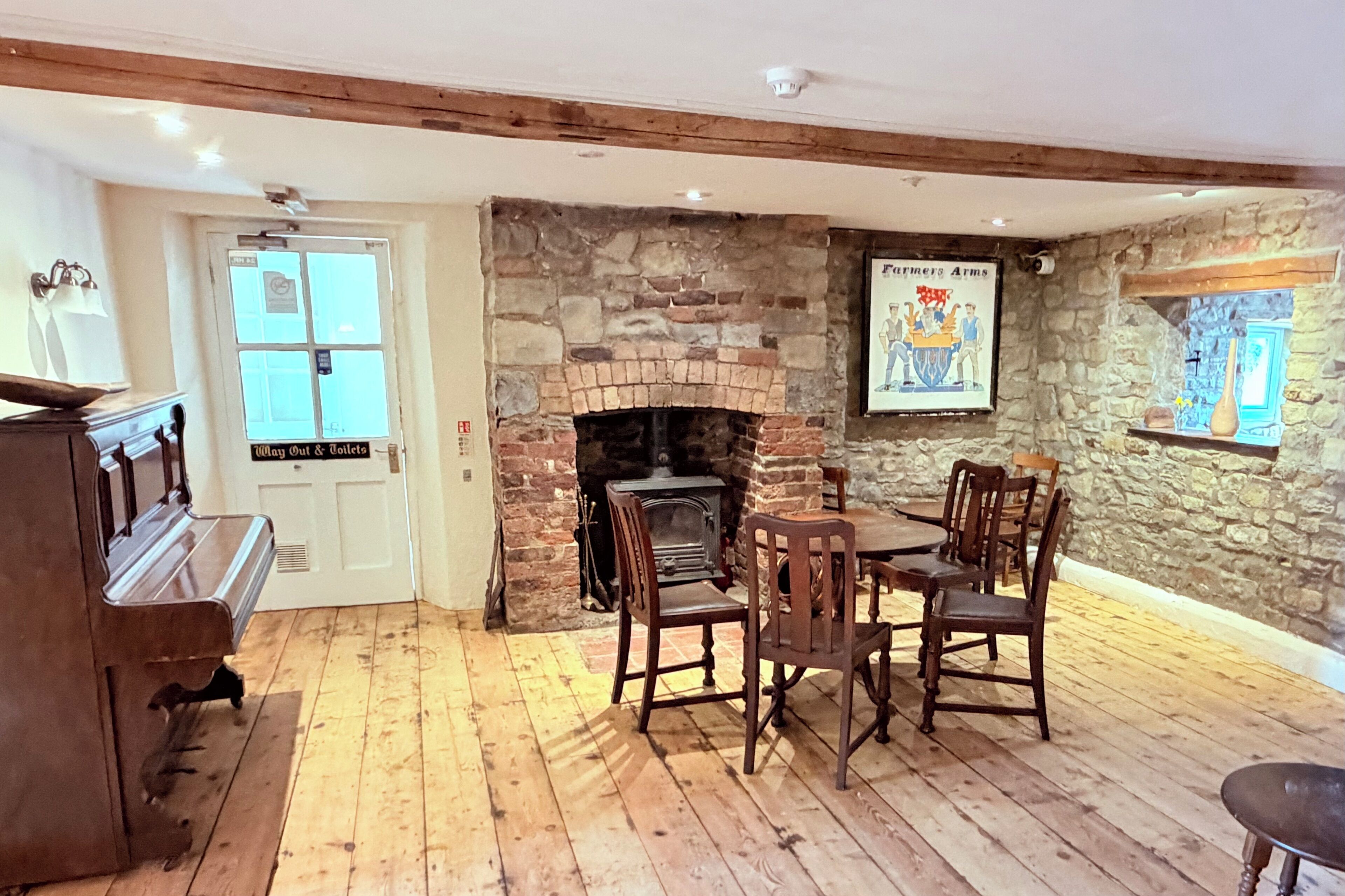 Una habitación con chimenea, suelo de madera, un piano y una mesa con sillas.