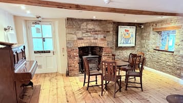 Una habitación con chimenea, suelo de madera, un piano y una mesa con sillas.