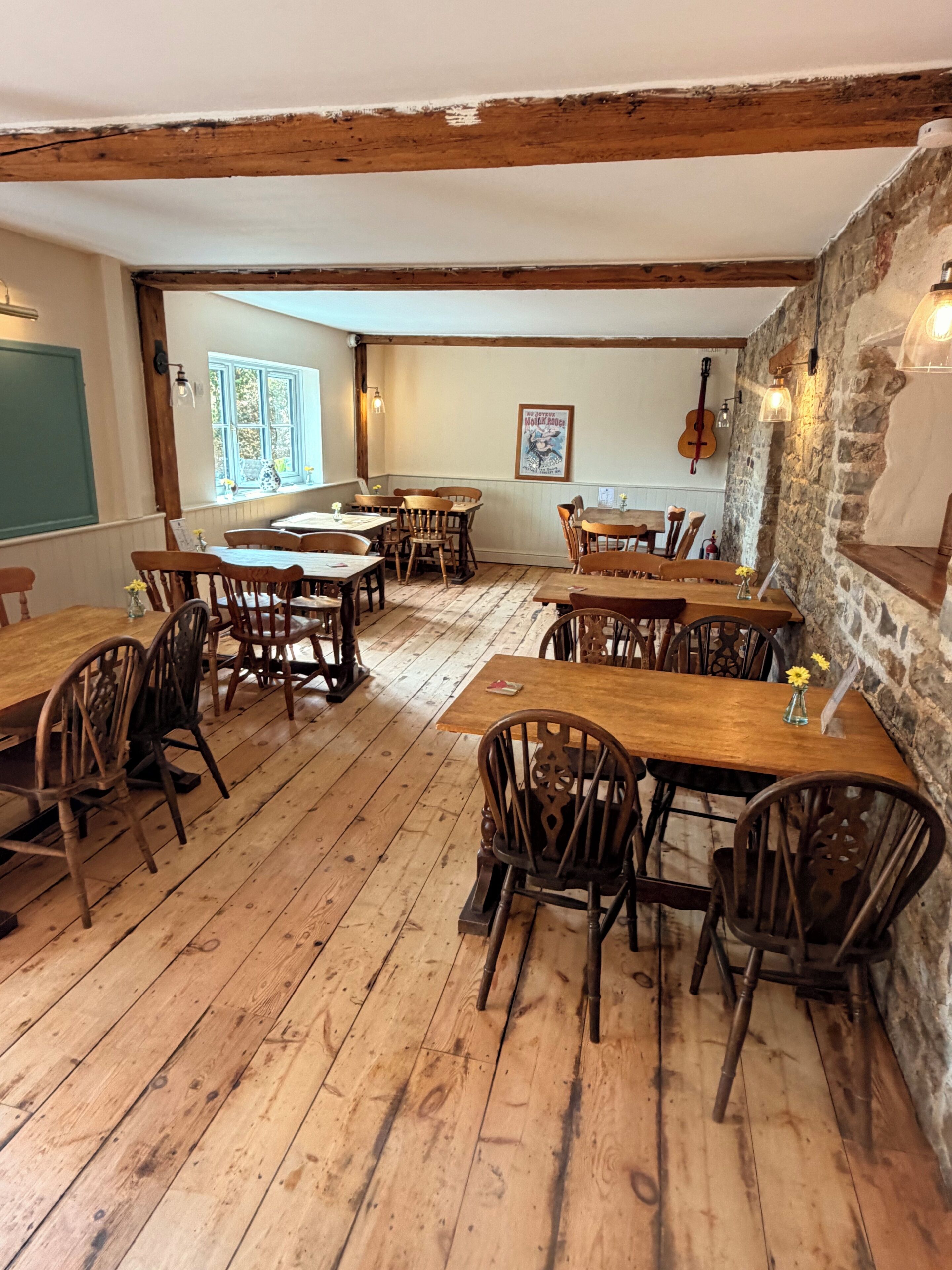 Un comedor rústico con mesas y sillas de madera, paredes de piedra y vistas al exterior.