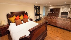 A bedroom with a wooden bed, a nightstand, a lamp, a patterned sofa, a stone wall, and a fireplace.