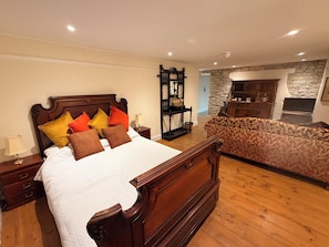 A bedroom with a wooden bed, a nightstand, a lamp, a patterned sofa, a stone wall, and a fireplace.