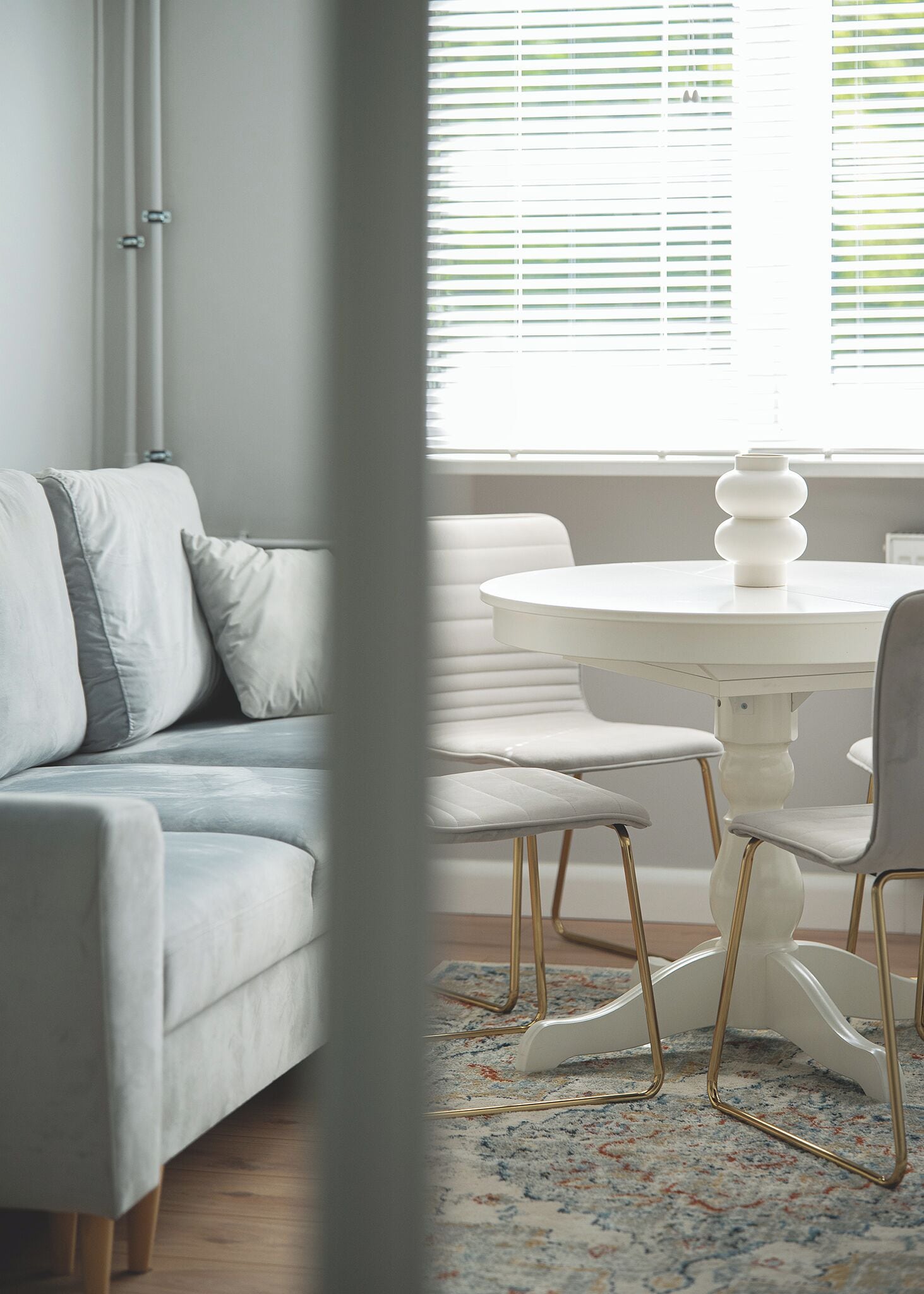 Una habitación con un sofá blanco, una mesa redonda con sillas y una ventana con persianas.