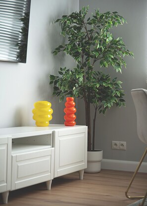 Un mueble blanco con dos objetos coloridos encima y una planta en maceta al lado.