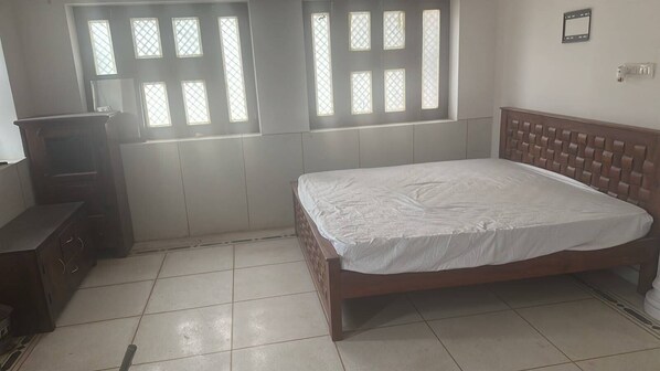 A bedroom with a bed, a dresser, and a window with blinds.
