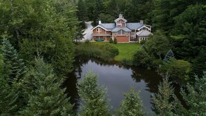 A large house surrounded by dense forest and a body of water. - Peak and Pond Mountain View Retreat hot tub theater sauna. (Killington)