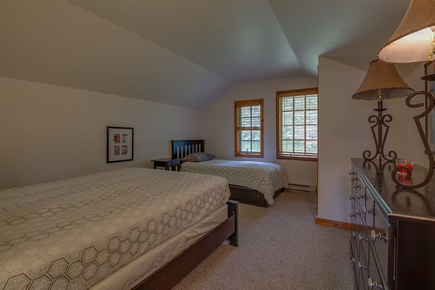 Un dormitorio con dos camas, un tocador, una lámpara y una ventana con persianas.