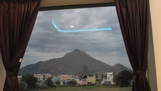 A window with curtains, a view of a mountain, and buildings in the foreground.