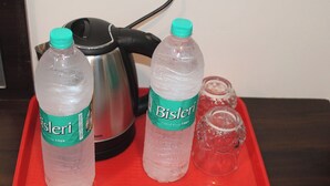 A tray with two Bisleri water bottles and a glass on a red tray, placed next to a kettle.